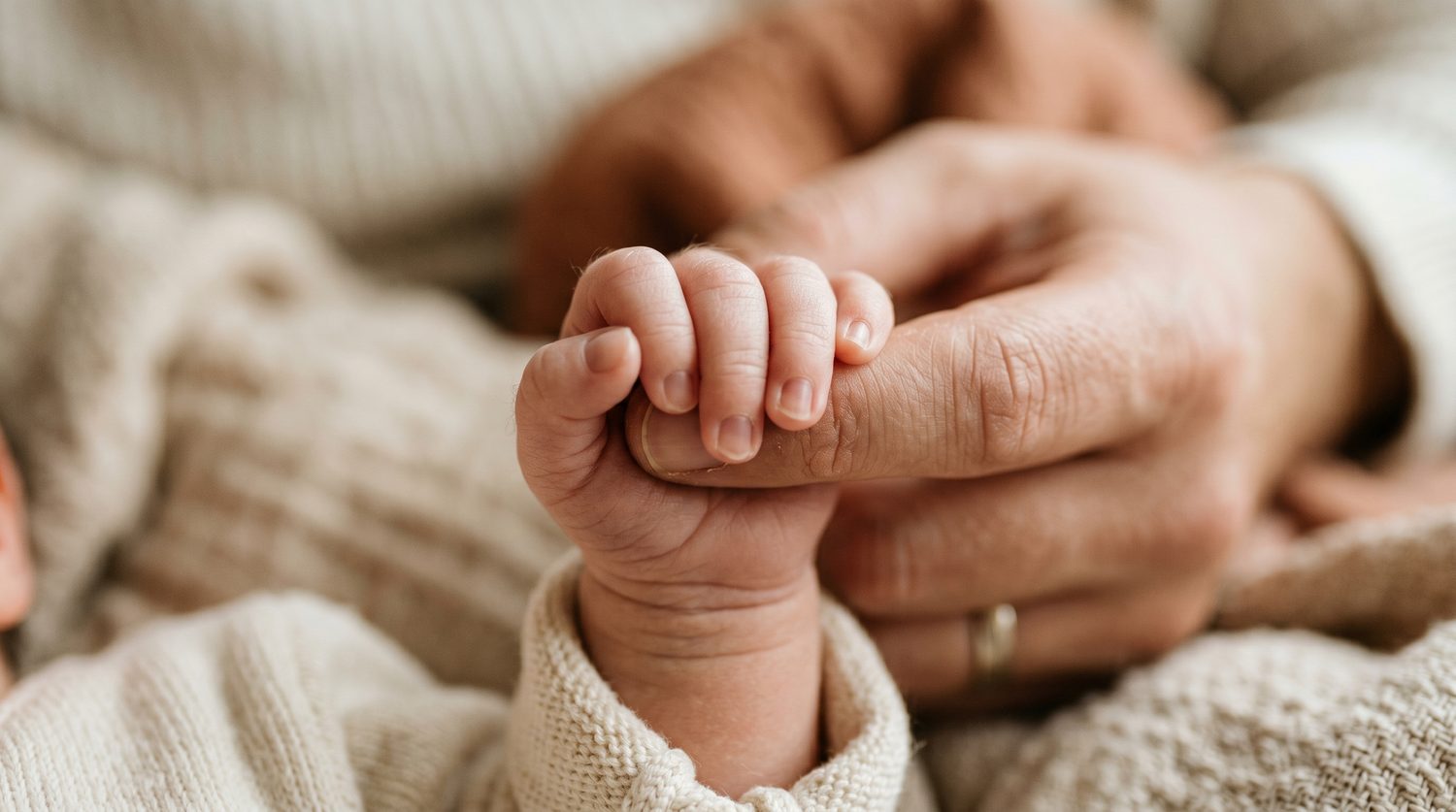 A newborn's hand curled around an adult's finger